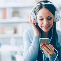 Młoda kobieta w słuchawkach słucha muzyki z telefonu, uśmiecha się.